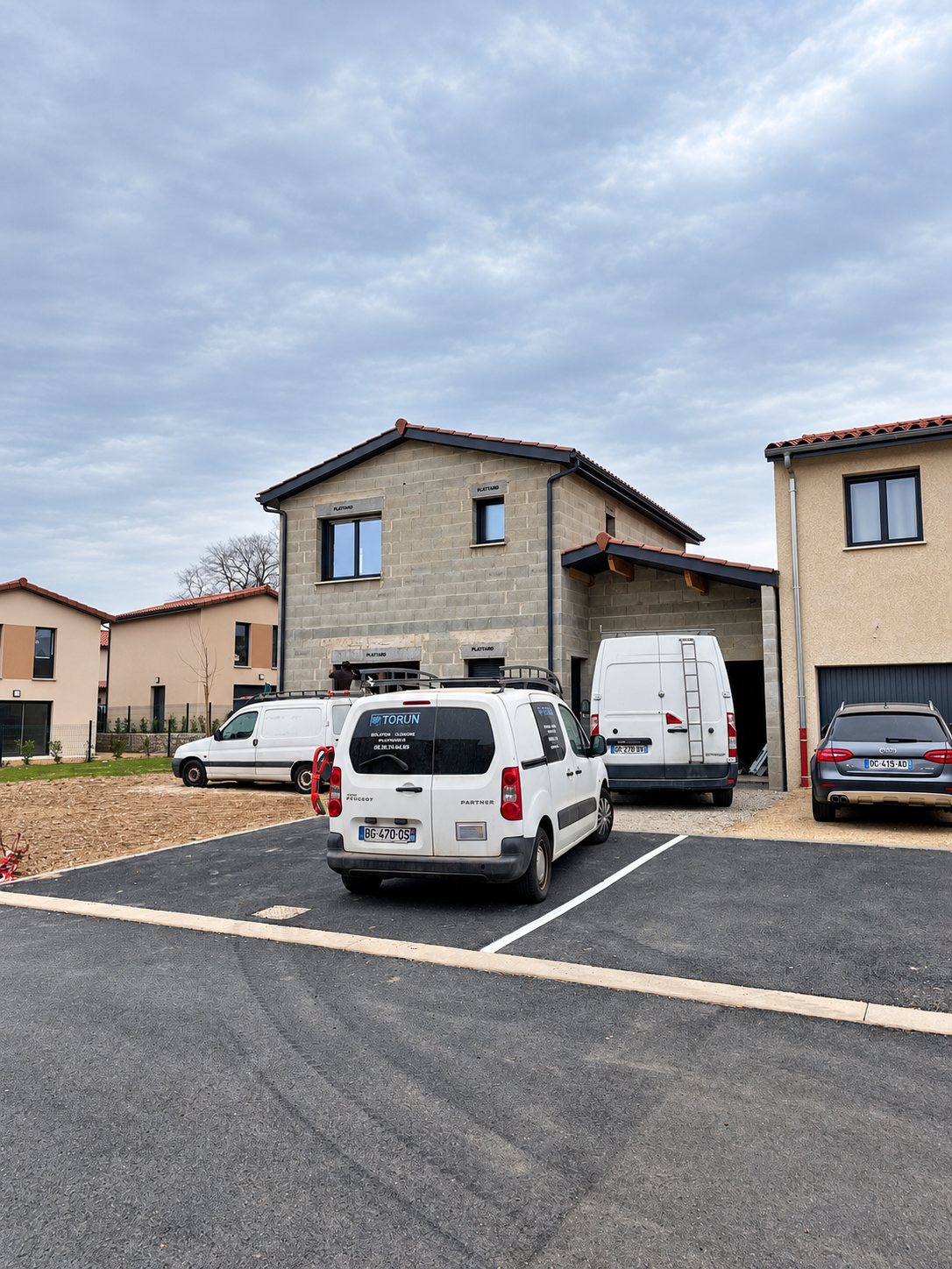 Trois camionnettes blanches de chantier devant des maisons de quartier résidentiel.