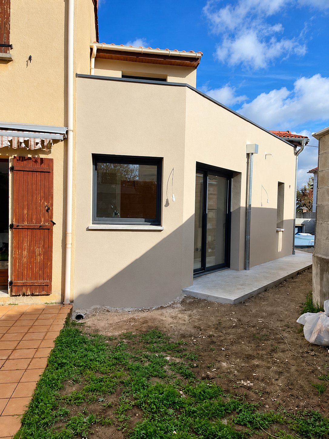 Extension moderne beige clair avec grandes fenêtres et baie vitrée coulissante.