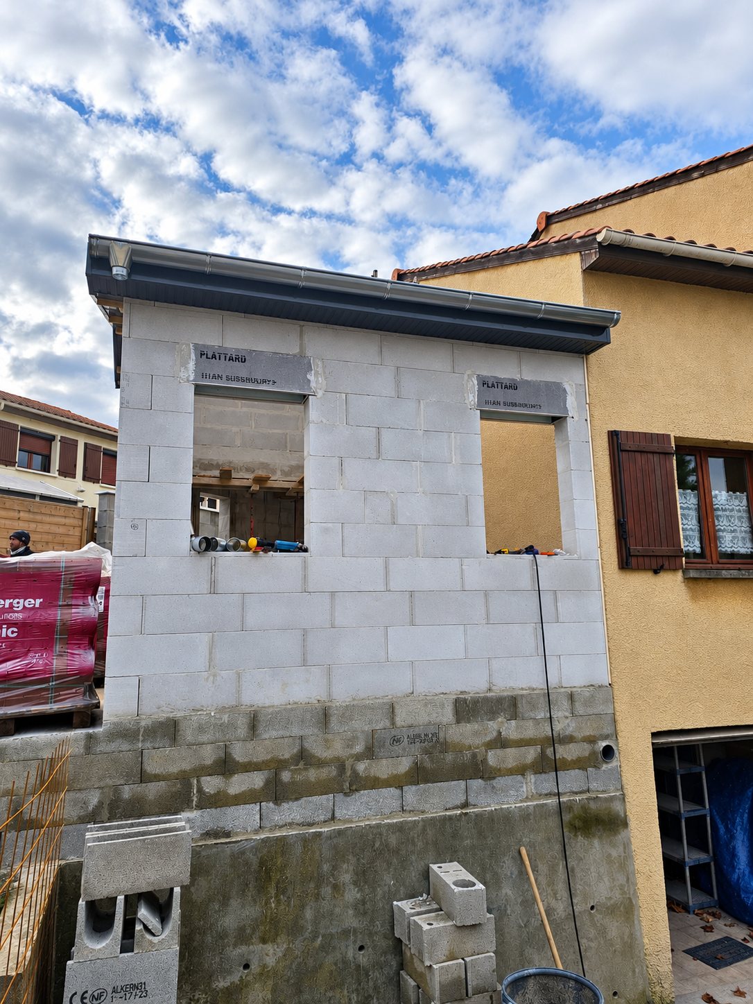 Extension de maison inachevée en parpaings blancs, avec deux ouvertures de fenêtres.