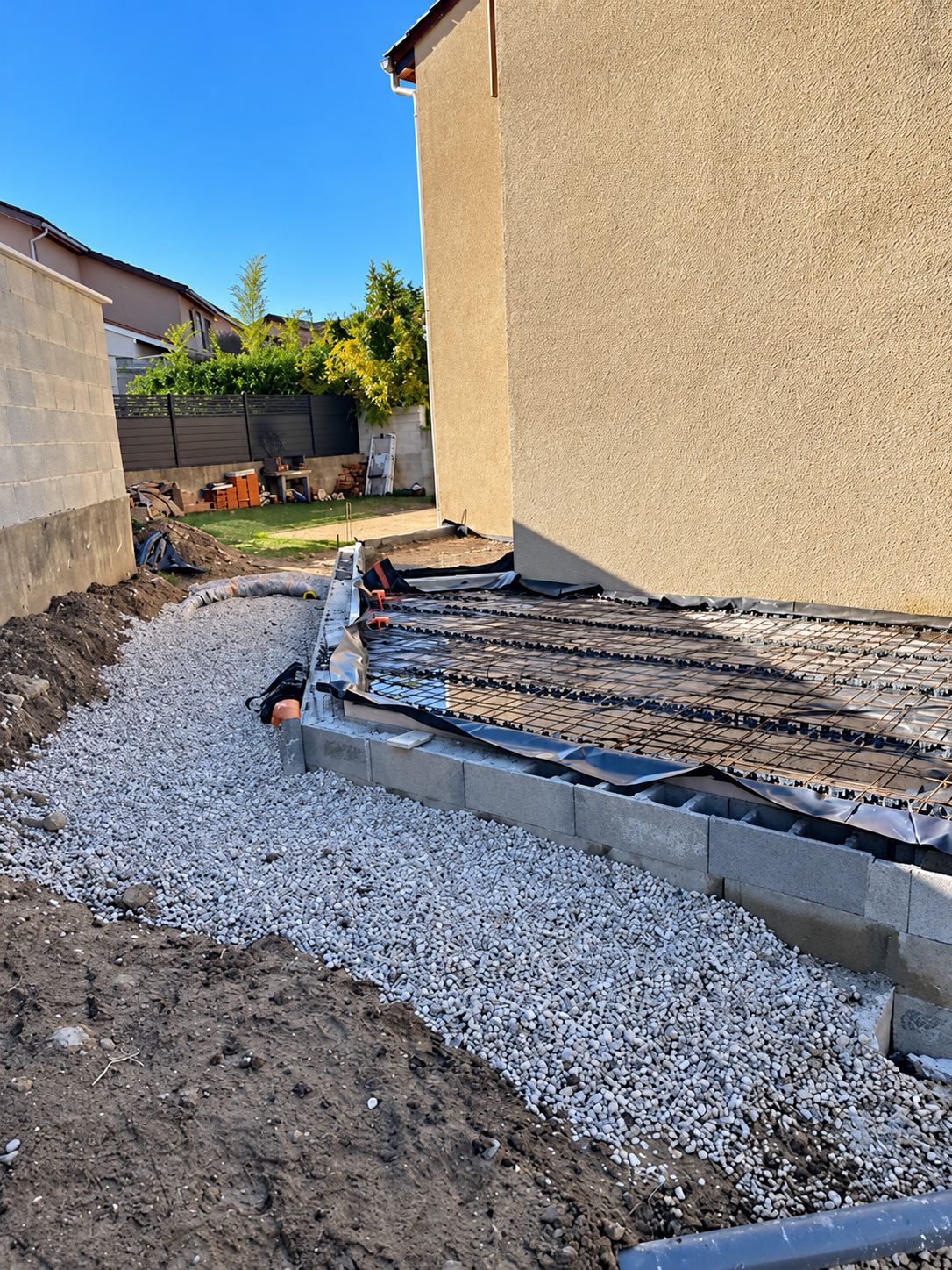 Fondation de chantier avec bordure en parpaings, treillis métallique et gravier.