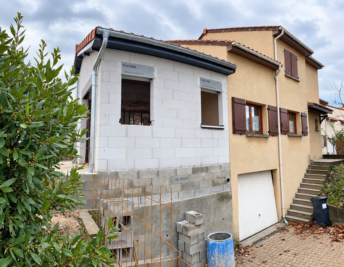 Maison beige à étage avec extension inachevée en parpaings blancs et garage.