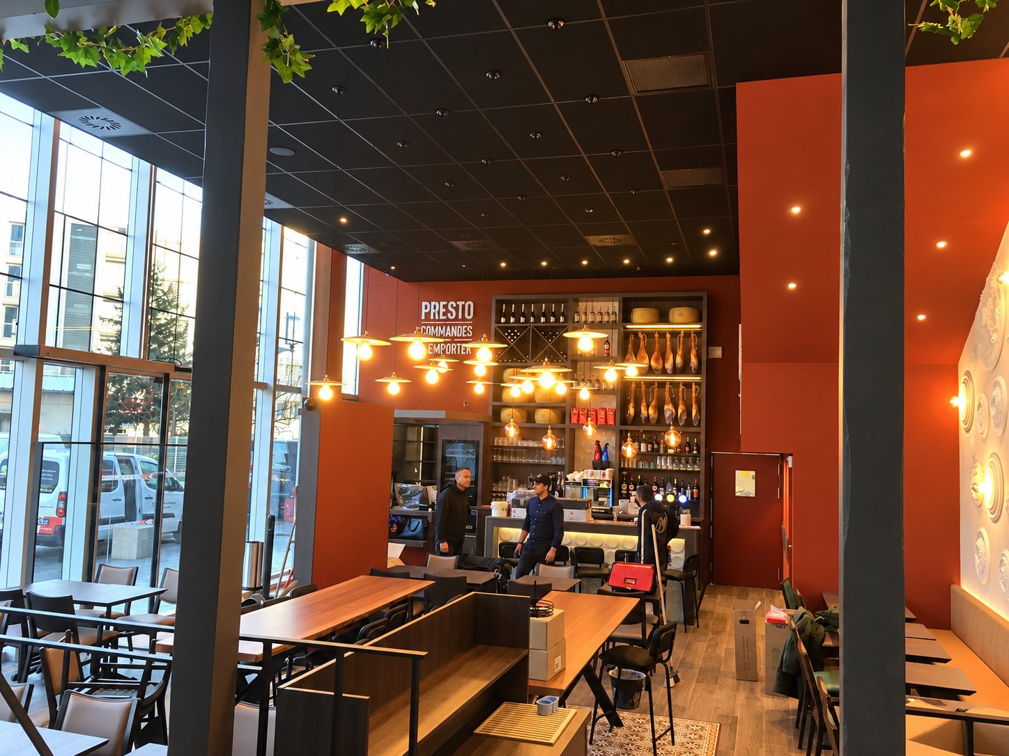 Salle de restaurant chaleureuse avec tables en bois, suspensions modernes et étagères de bar.